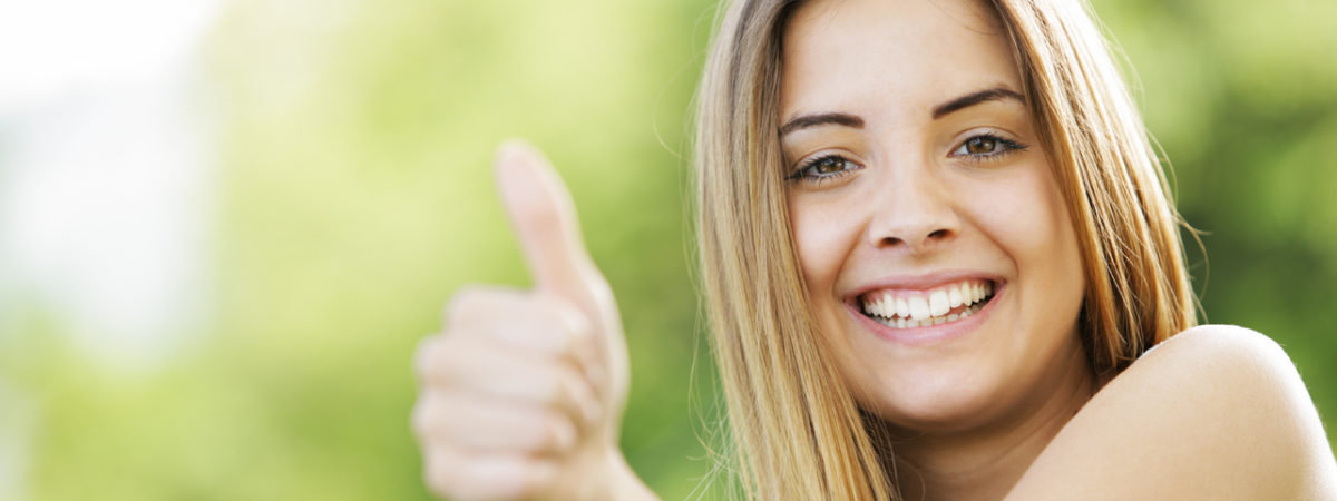 Smiling young woman giving a thumbs up outdoors