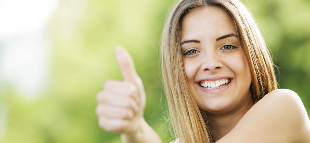 Smiling young woman giving a thumbs up outdoors