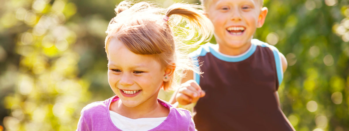Two smiling children running outdoors on a sunny day