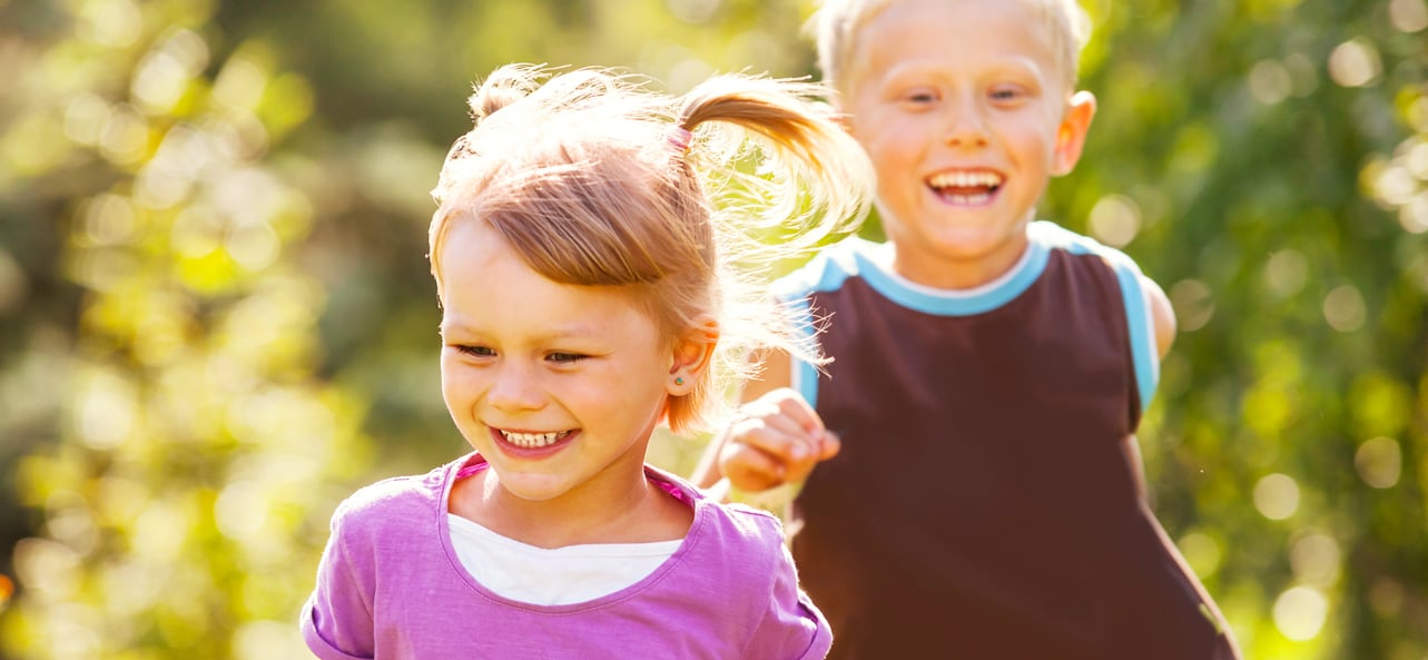 Two smiling children running outdoors on a sunny day